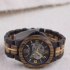 Black and gold transparent round skeletonized wooden men's automatic winding wooden watch with gold hands.