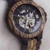Black and gold transparent round skeletonized wooden men's automatic winding wooden watch with gold hands.